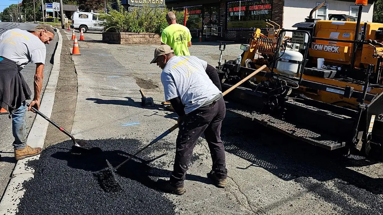 Paving crew raking hot asphalt into a repair patch on a commercial frontage